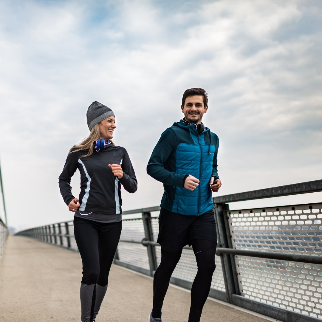 Two people jogging on a bridge with a cloudy sky.