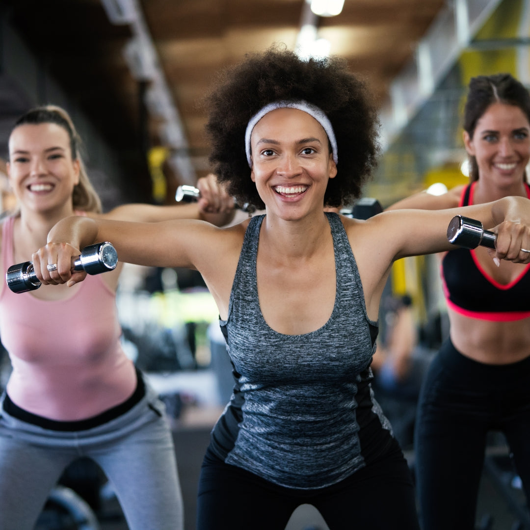 Three women exercising with dumbbells in a gym setting