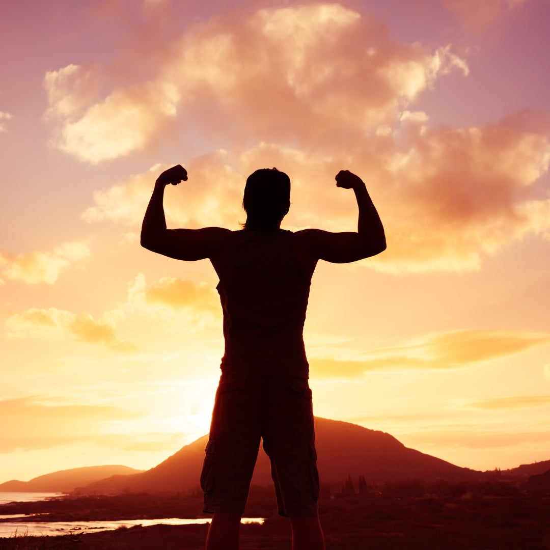 Person flexing muscles against a sunset sky